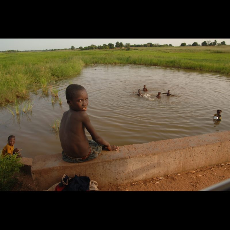 KONADOUGA, Burkina Faso — A young boy sits on a bridge in the village of Konadouga, where he and his friends are playing in the water.
