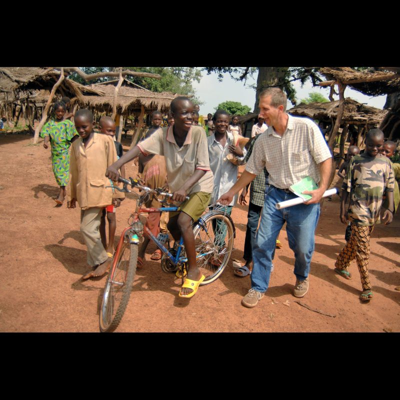 DAKORO, Burkina Faso — David Wood holds a boy’s bicycle as they play together, surrounded by curious children from the community in Dakoro, a Senara village. David and Tami Wood walked through the town, building relationships and connecting with local families.