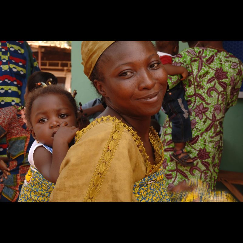 OUAGADOUGOU, Burkina Faso — A young mother carries her child on her back in front of Bon Berger (Good Shepherd) Baptist Church in Ouagadougou, Burkina Faso. The church serves as a spiritual and community center for many local families.