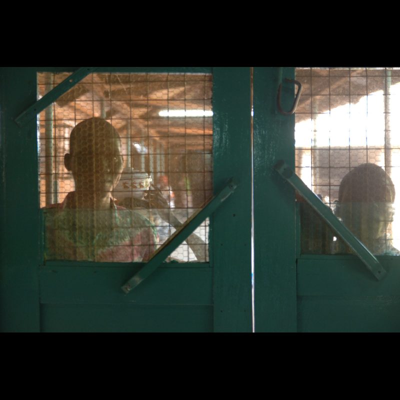 NALERIGU, Ghana — Two men stand outside, looking through a screen door while waiting for visiting hours at the Baptist Medical Center in Nalerigu, Ghana. The hospital is a key medical care provider for communities throughout northern Ghana.